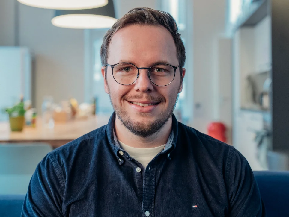 Porträt von Johannes Kunze, lächelnd mit Brille in einem hellen Büro.