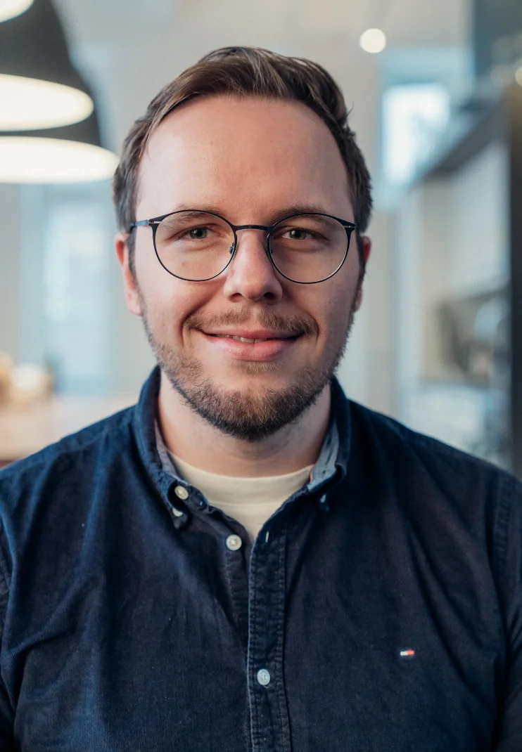 Porträt von Johannes Kunze, lächelnd mit Brille in einem hellen Büro.